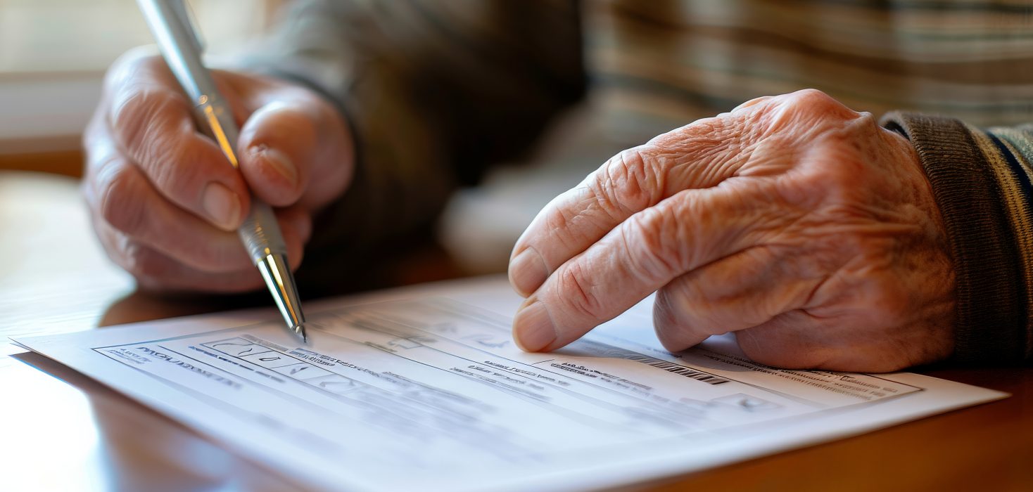 Elderly person filling out a form with a pen, showing aged hands and focus on writing