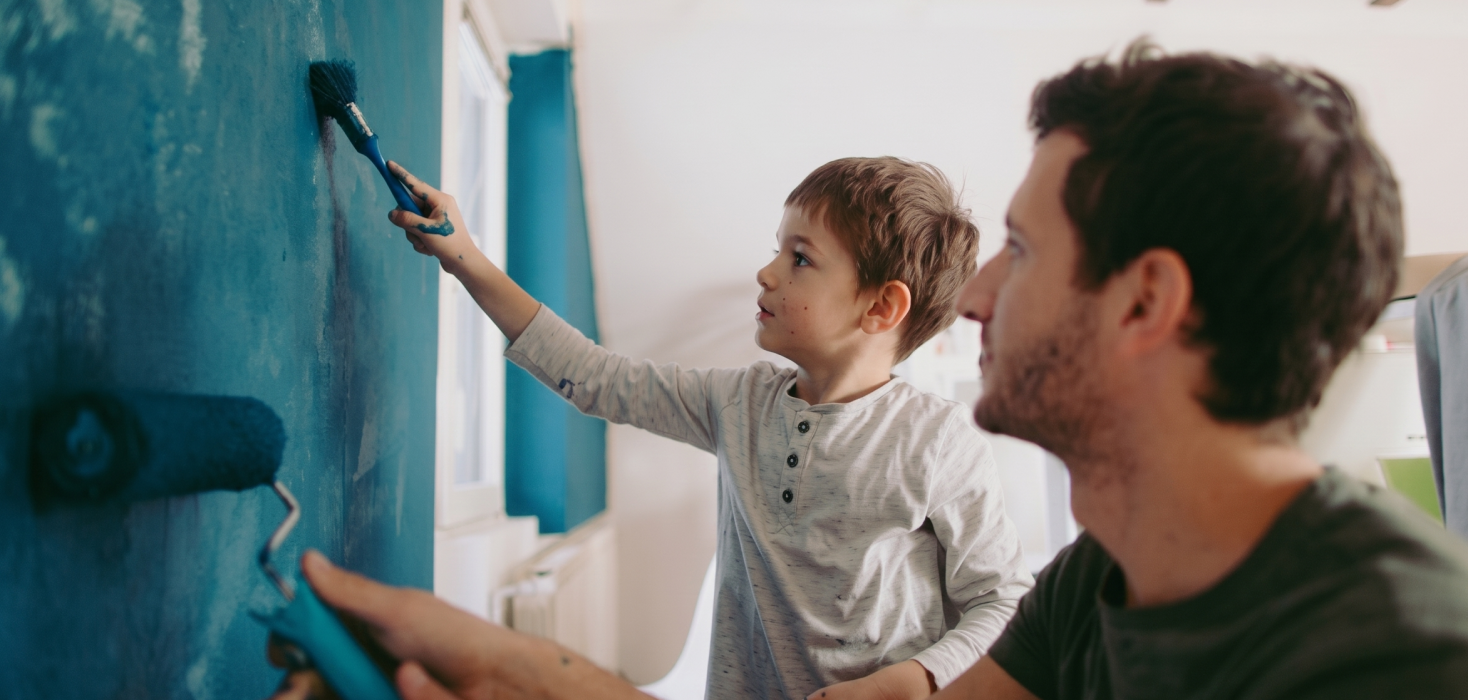 Father and son painting a wall blue together at home, bonding during a DIY project