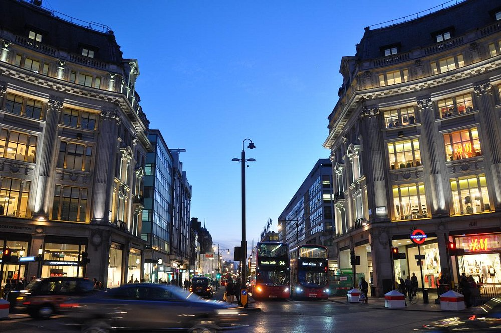 A busy street scene at dusk, showcasing cars and pedestrians moving amidst the evening glow